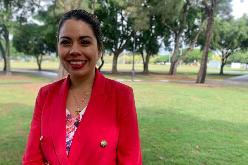 Woman in pink jacket over a floral dress standing in park