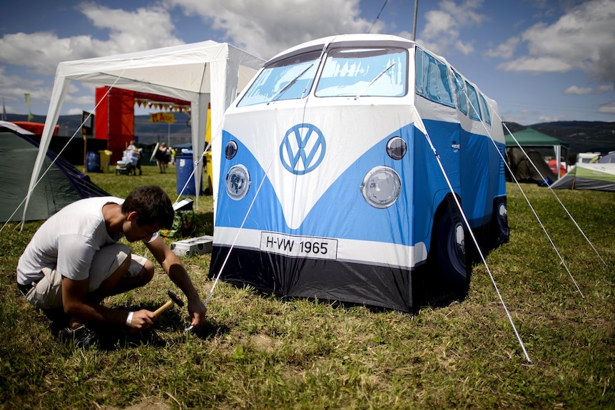 A man erects a Kombi van-shaped tent at a music festival.