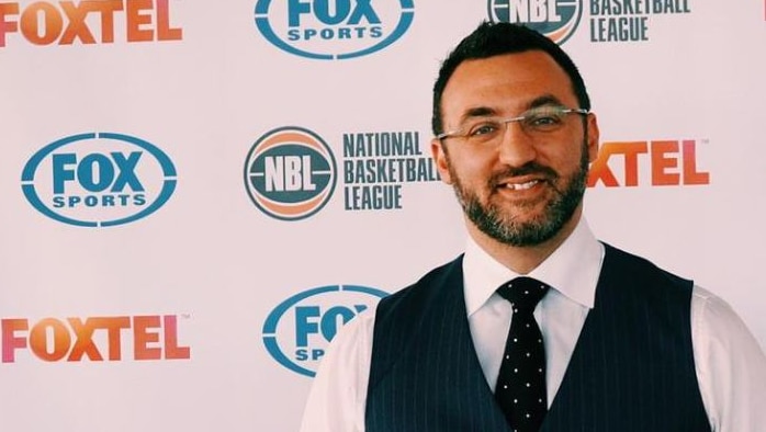 NBL CEO Jeremy Loeliger stands holding a basketball in front of a media wall.