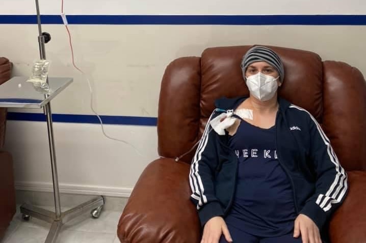 A woman sits in a brown armchair hooked up to an IV drip with stem cells.