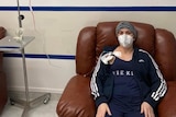 A woman sits in a brown armchair hooked up to an IV drip with stem cells.