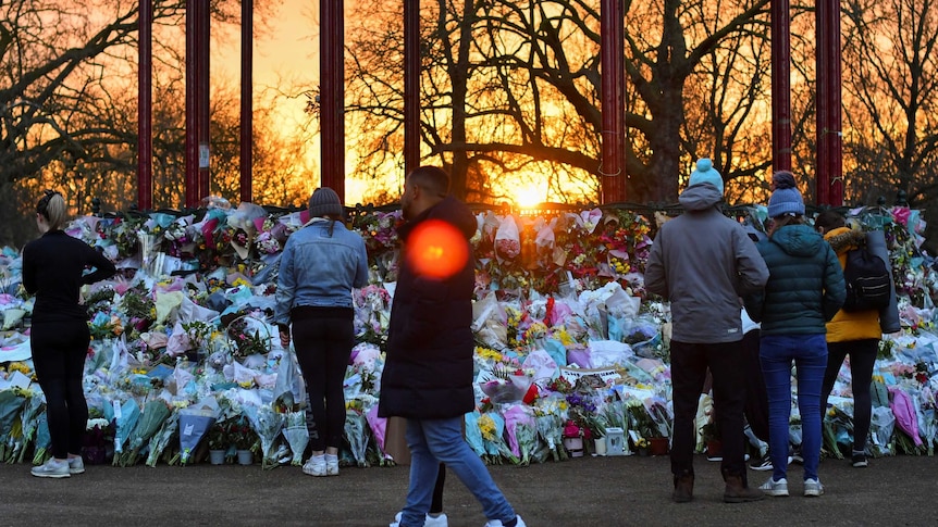 People walk past a huge bunch of flowers at sunset