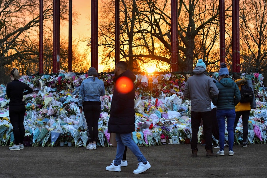 People walking past a huge pile of flowers as the sun sets