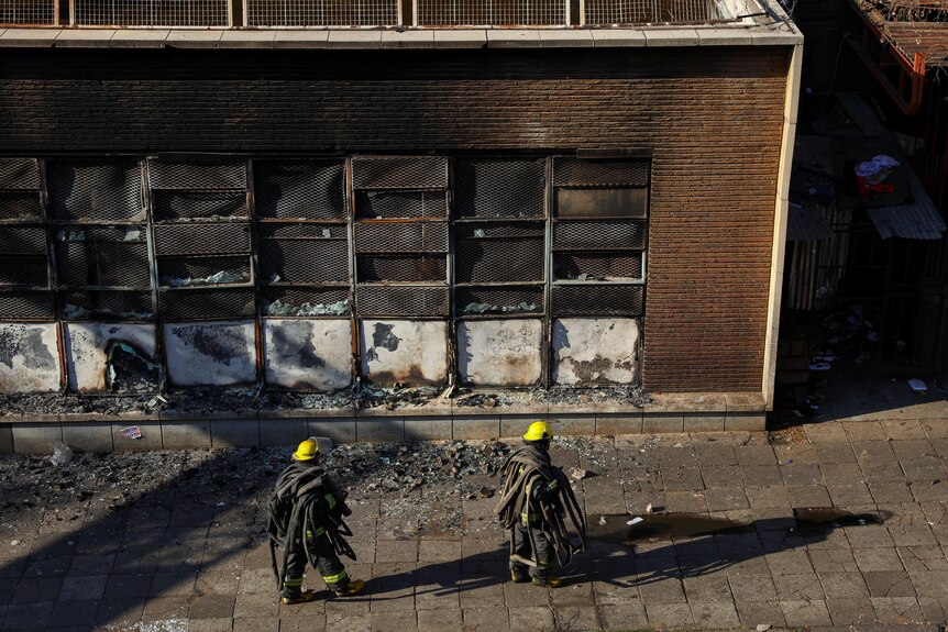 Firefighters walk next to burnt out building 