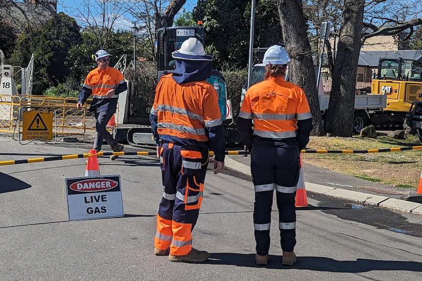 Three workers in bright orange high-vis gear on a street.