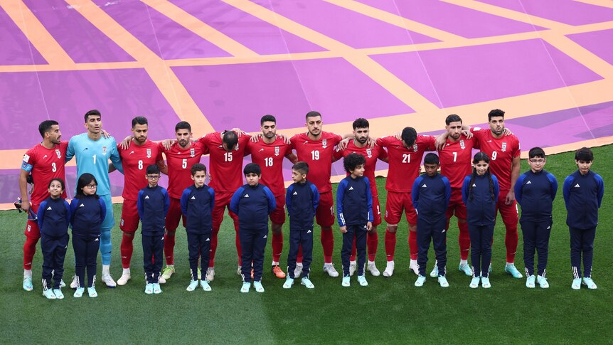 Footballs players are dressed in red standing in a line with their arms around each other's shoulders. 