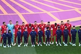Footballs players are dressed in red standing in a line with their arms around each other's shoulders. 