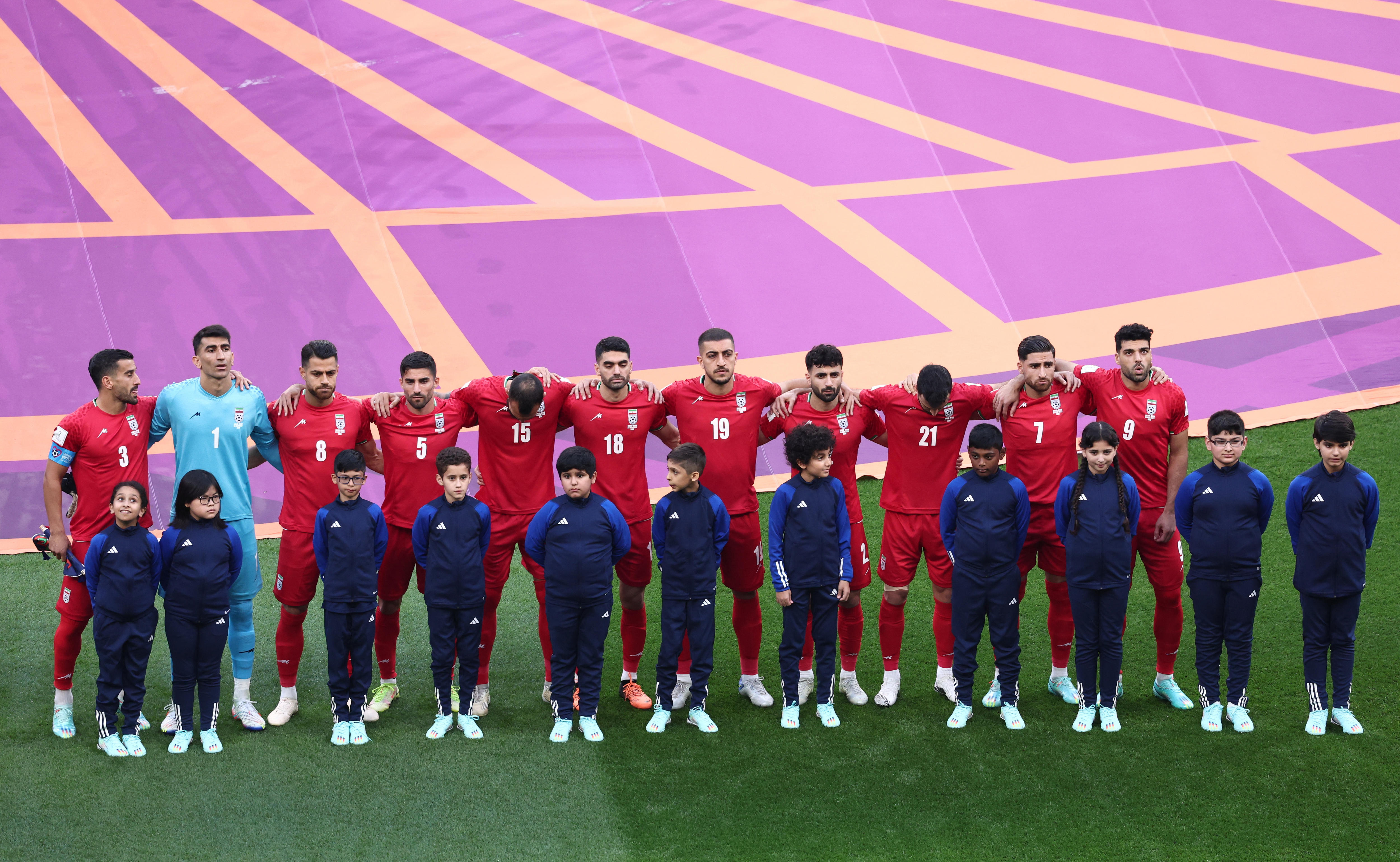 足球运动员身穿红色衣服，双臂搂着对方的肩膀站成一排。 