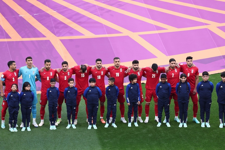 Footballs players are dressed in red standing in a line with their arms around each other's shoulders. 