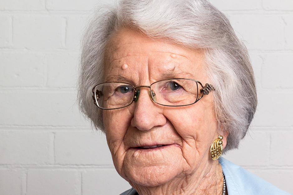 An elderly woman in front of a white wall.