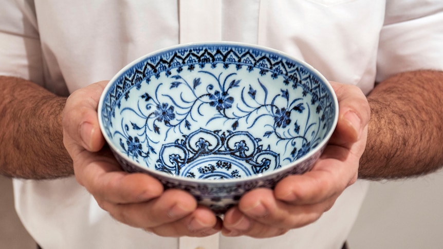 A bowl decorated with blue patterns and flowers held in a man's hands.