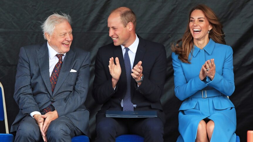 David Attenborough, Prince William and Catherine, Duchess of Cambridge sit together clapping and laughing.