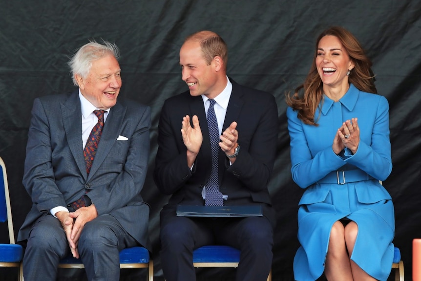 David Attenborough, Prince William and Catherine, Duchess of Cambridge sit together clapping and laughing.