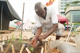 A man squats in a garden as he uses his hands to plant seeds in the soil.