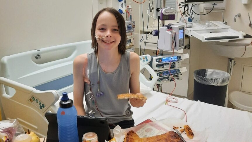 boy sitting on hospital bed, smiling, eating pizza