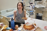 boy sitting on hospital bed, smiling, eating pizza