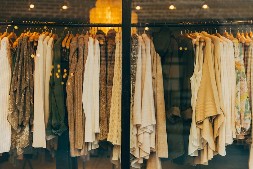 A rack of clothing in a store, mostly jumpers and autumnal knits.