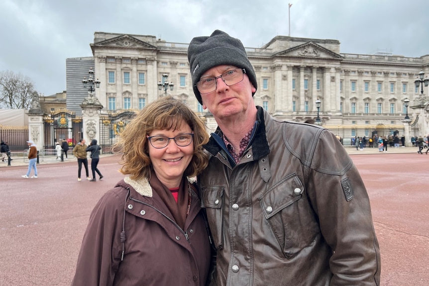 A woman and man dressed in coats outside Buckingham Palace.
