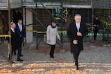 Scott Morrison, wearing a long winter jacket, walks out of a construction site followed by two men and a woman.