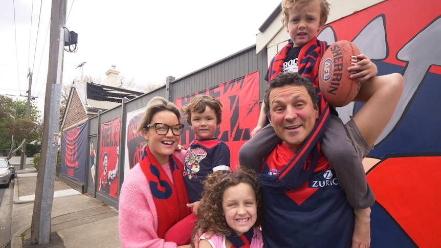 Ted Dohrmann stands with his wife and children in front of a mural of Melbourne footy murals.