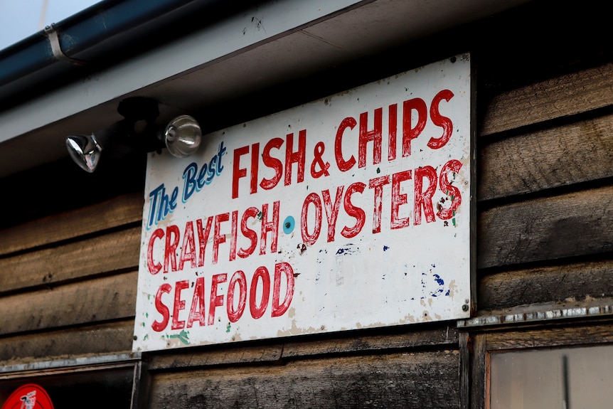 Old faded painted sign advertising Fish and chips on wooden slats 