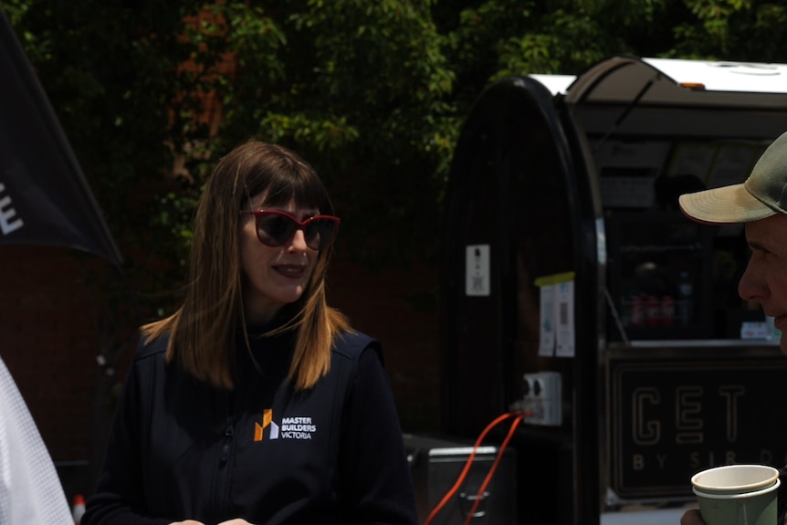 A woman speaks to a man holding a coffee cup