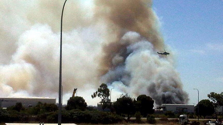 A helicopter flies off after dropping water on a bushfire at Kewdale.