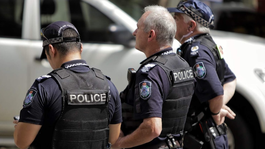 Three unidentified Queensland Police officers stand in a row.