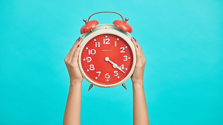 Person holds up a red alarm clock against a bright blue background.
