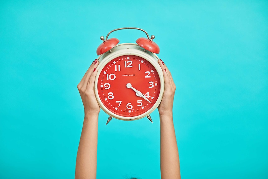Person holds up a red alarm clock against a bright blue background.