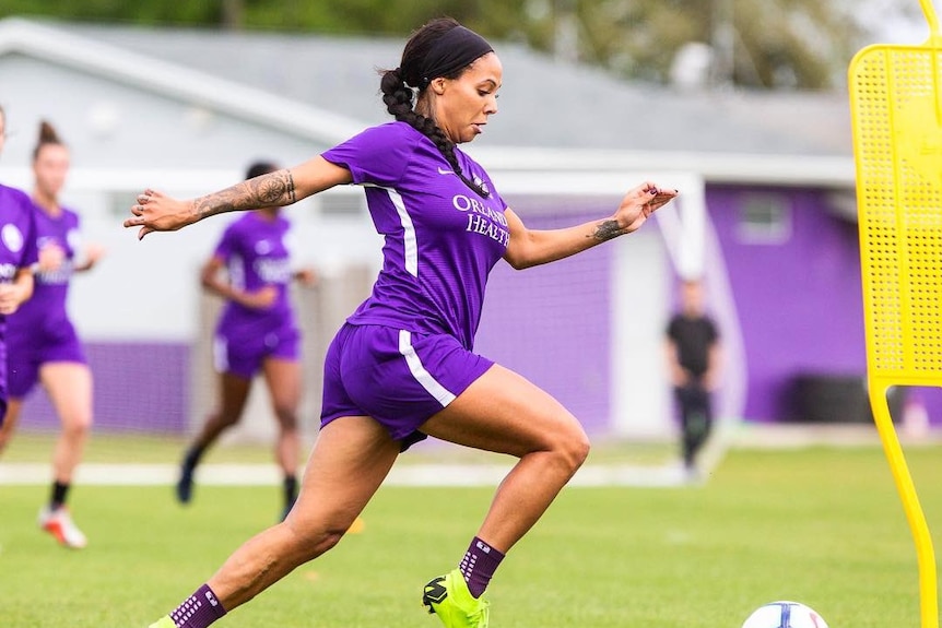 Sydney Leroux Dwyer running at training with teammates in the background and a ball at her feet.