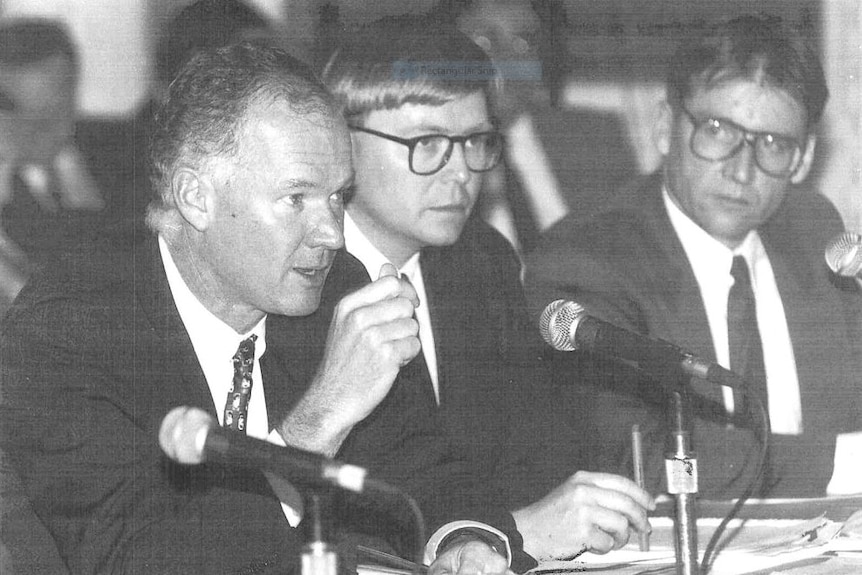 Black and white image of three men speaking into microphones.