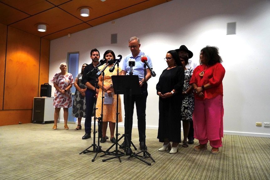 Anthony Albanese speaks at a podium with several people on either side of him. 