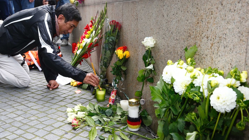 man lights incense sticks near flowers laid for victims of the Munich attack