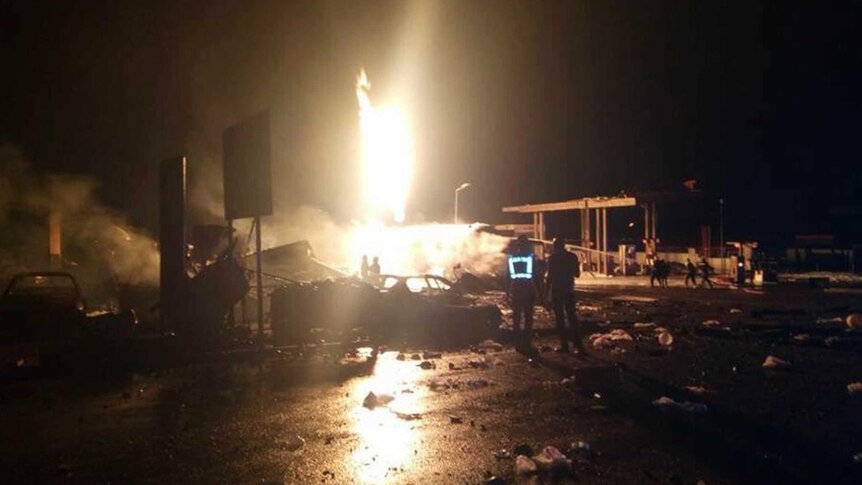 People gather in the dark watching a bright explosion at a petrol station in Ghana.