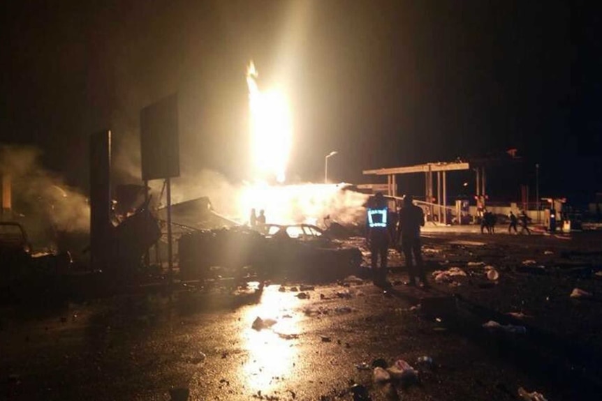 People gather in the dark watching a bright explosion at a petrol station in Ghana.