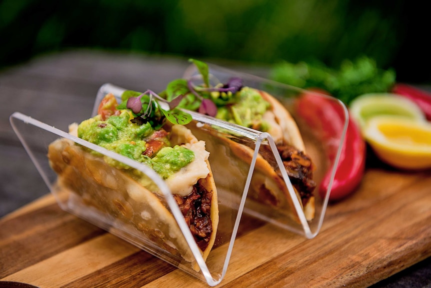 Tacos, filled with meet and avocado, sitting in a plastic stand.