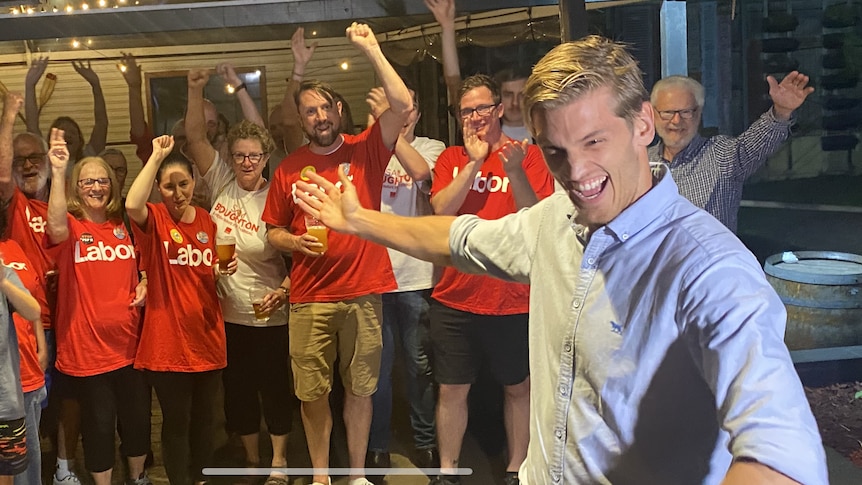 man in collard shirt celebrates with people wearing red shirt surrounding him, clapping