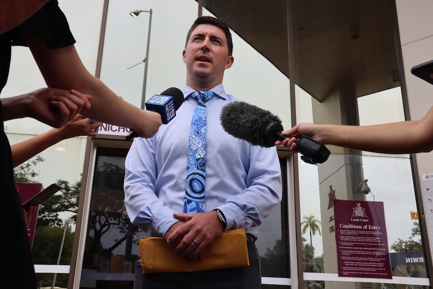 A man wearing a blue shirt and tie talks to the media outside of Darwin Local Court.