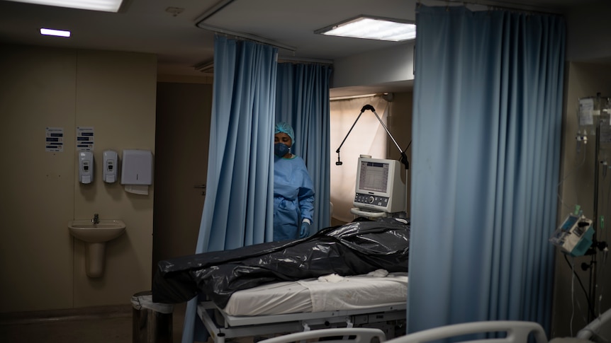 A nurse stands beside a black body bag in a modern hospital ward.