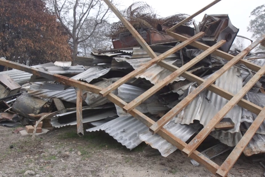 Burnt metal, wood and fixtures sit in a pile in daytime light.