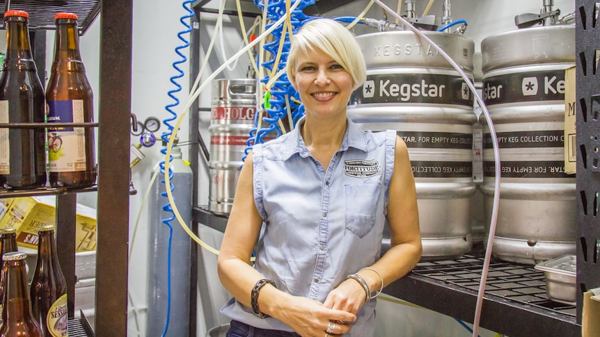 A women standing in a cold room with beer kegs.