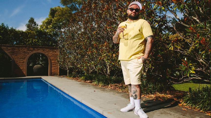 A 2019 press shot of Briggs rocking a tee and white sneakers poolside with a cocktail