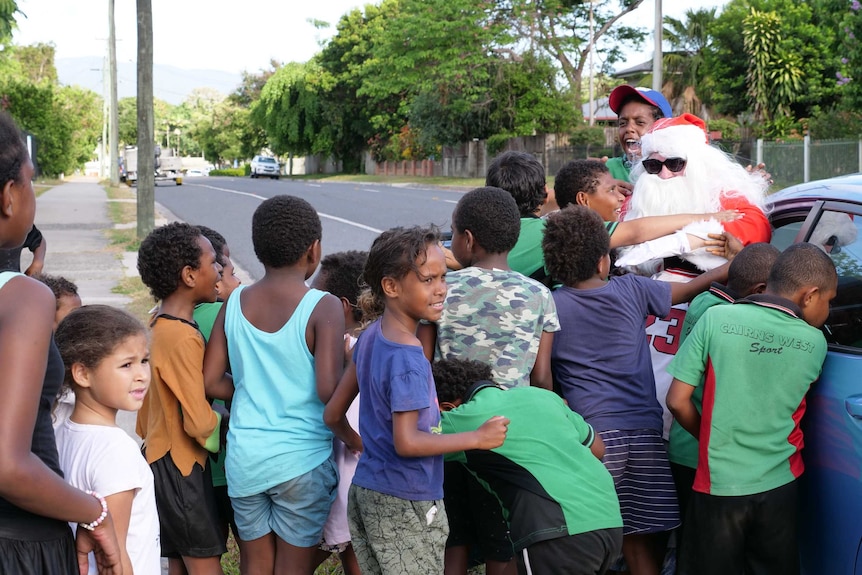Group of mainly Indigenous children hug a person dressed in a Santa Claus suit getting out of a car