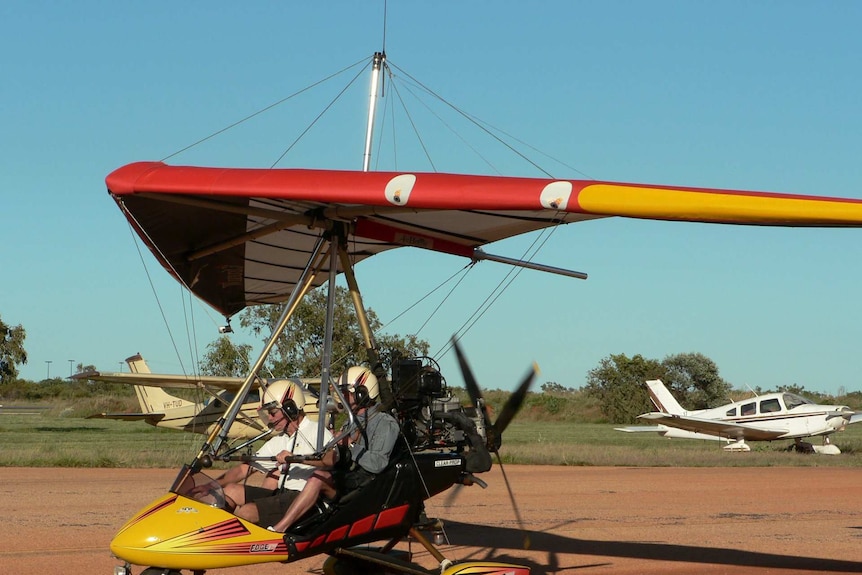 Two men sit in an ultra-light aircraft as it moves along a runway