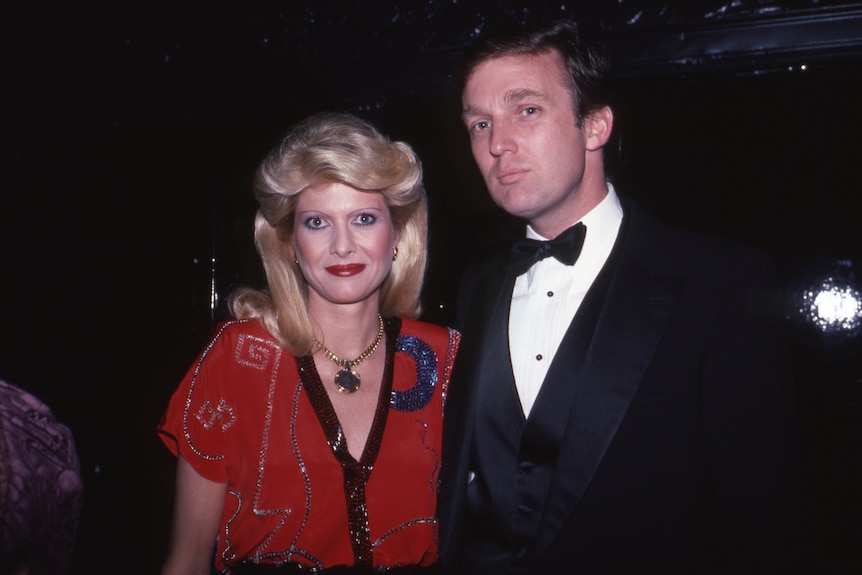 A young, blonde woman in a red and black dress is accompanied by a young man in a dark suit and bow tie.