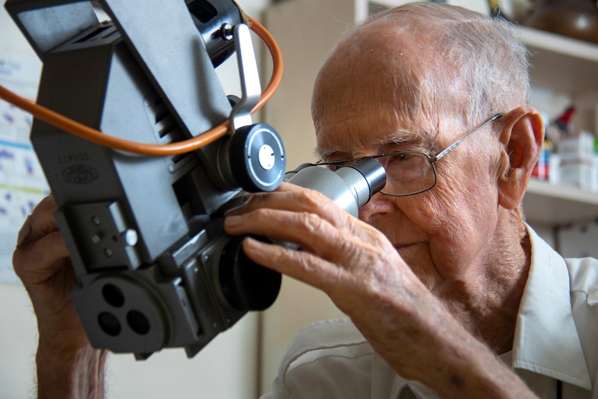 An old man looks into a vintage looking medical microscope.