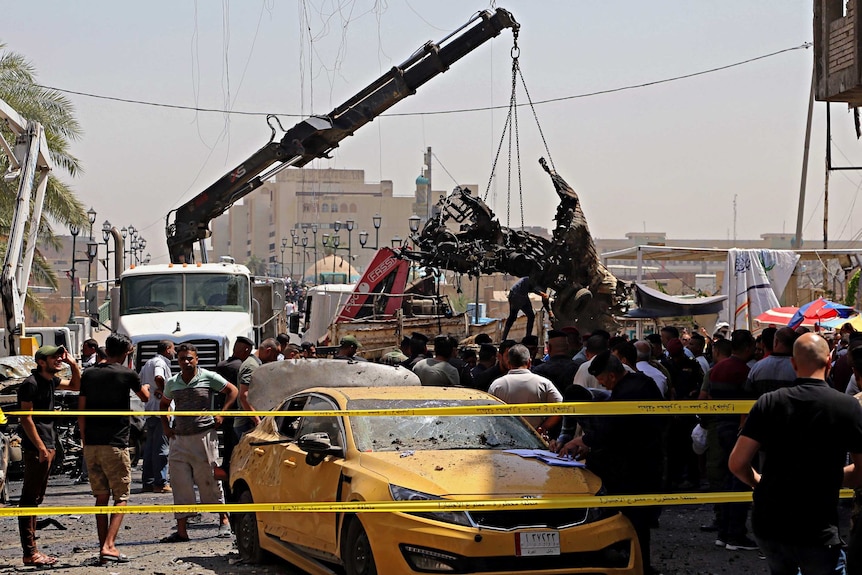 A crane lifts a burnt-out car in a crowded area of Baghdad at the site of a car bomb attack.