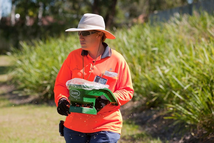 woman in high-vis with a fire ant bait spreader
