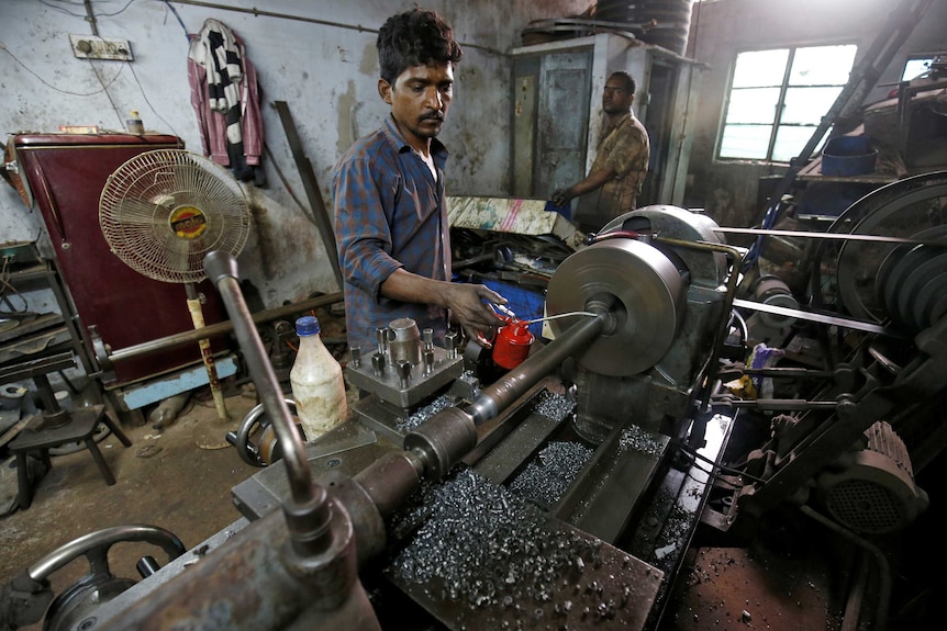 A man stands working at a piece of machinery in an Indian factory.